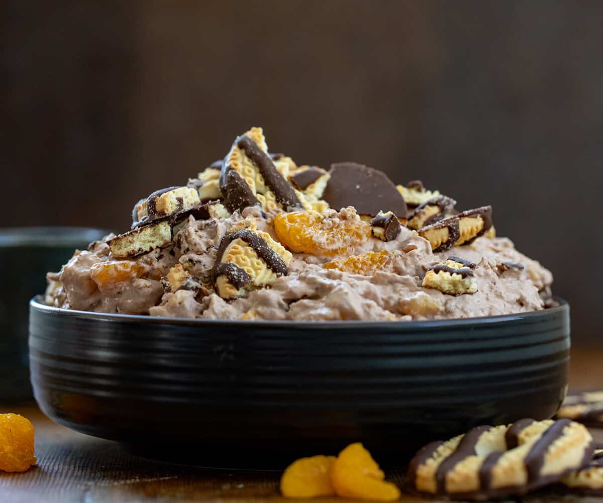 Bowl of Chocolate Cookie Salad on a wooden table with fudge strips cookies and mandrin oranges with a straight on view.