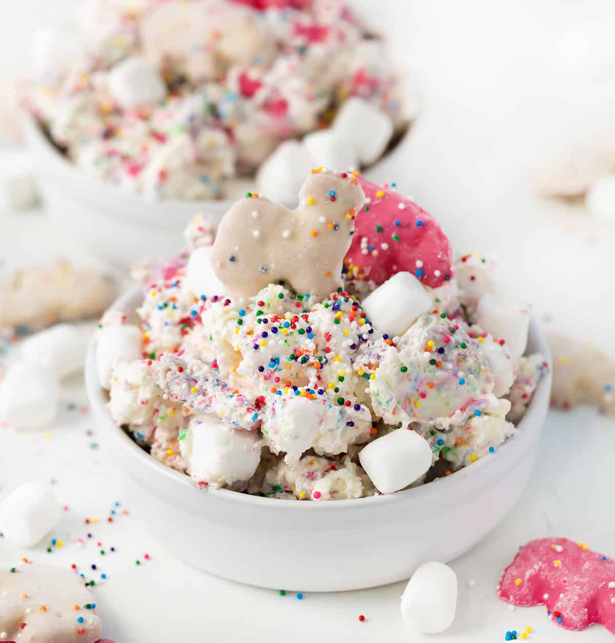 Bowls of Circus Cookie Salad Fluff on a white counter with rainbow non perils and mini marshmallows all around.