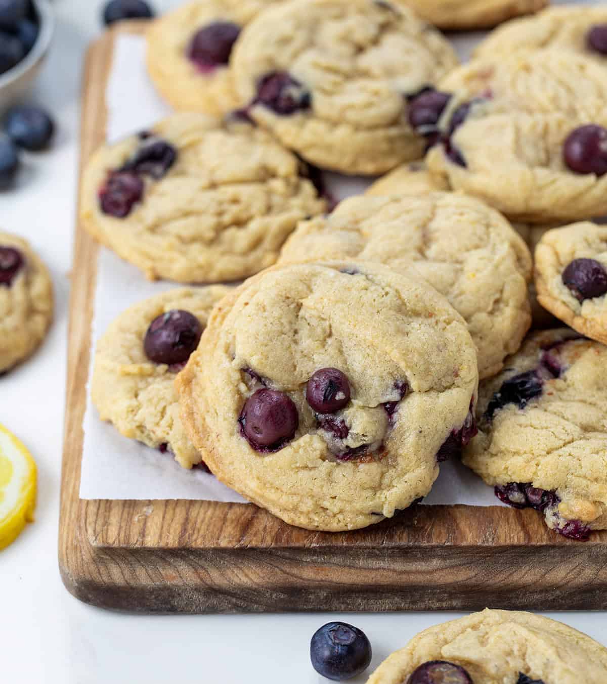 Lemon Blueberry Cookies on a cutting board stacked with fresh blueberries and lemon slices.
