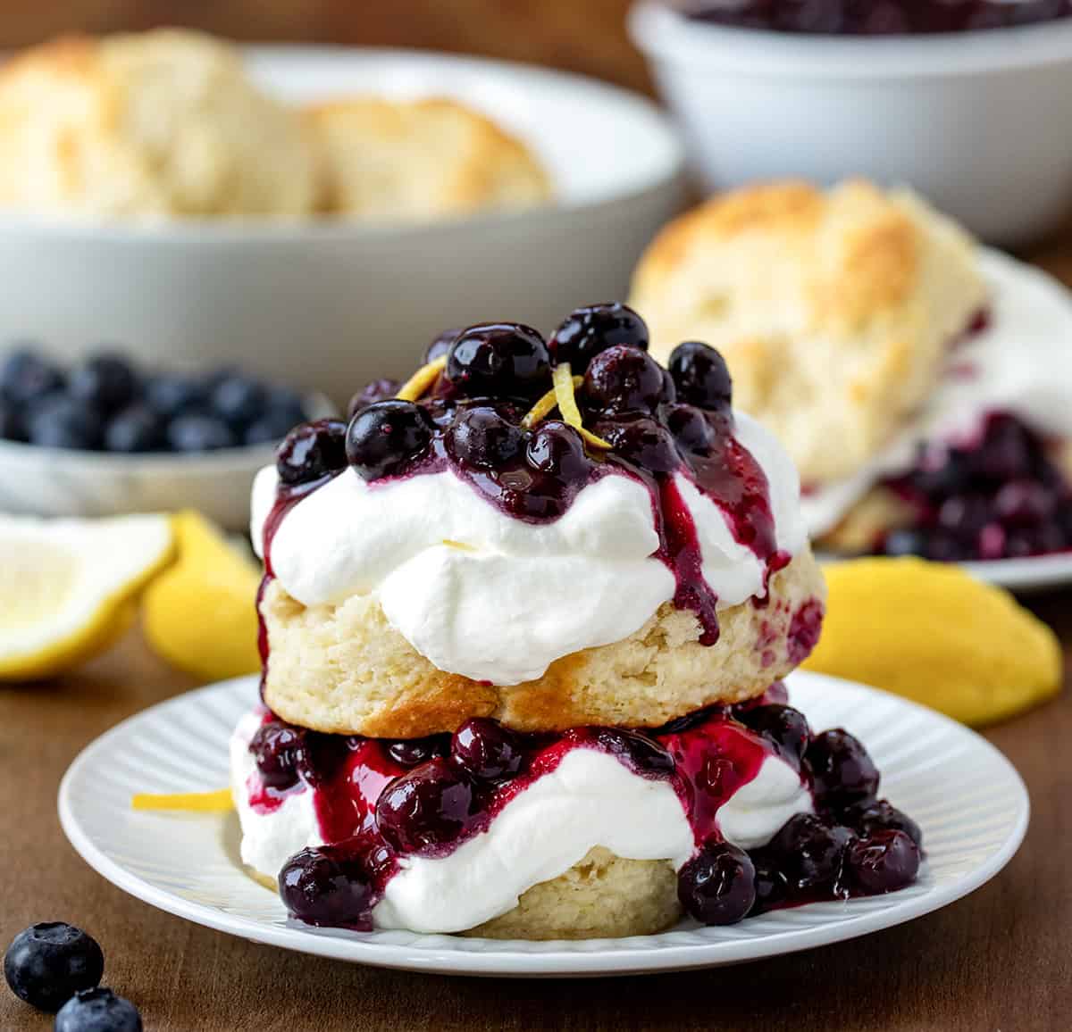 Lemon Blueberry Shortcake on a white plate with lemon zest and more ingredients in background.