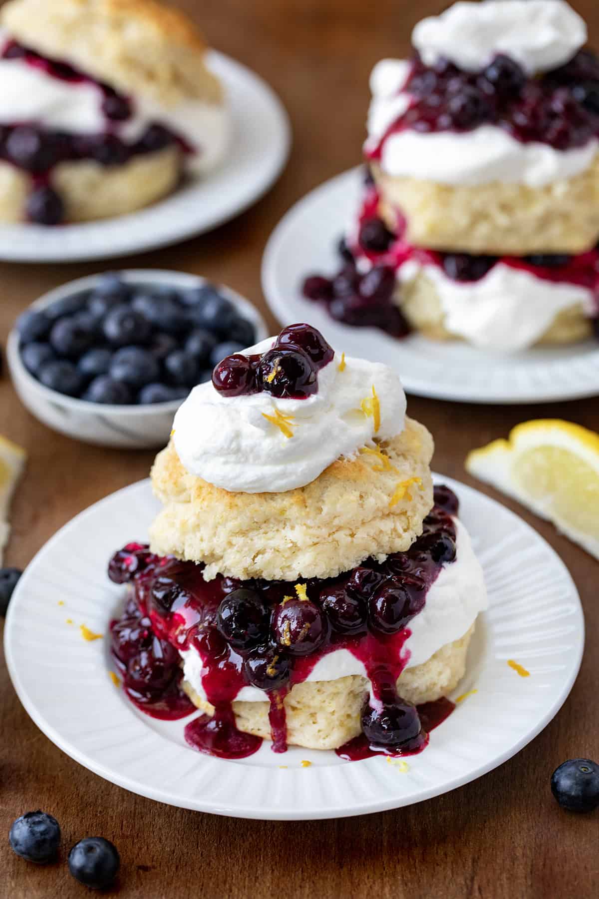Two Lemon Blueberry Shortcake on white plates surrounded by fresh blueberries and lemon wedges. 