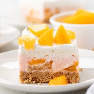 One piece of Peach Delight Dessert on a white plate with more in background.