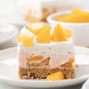 One piece of Peach Delight Dessert on a white plate with more in background.