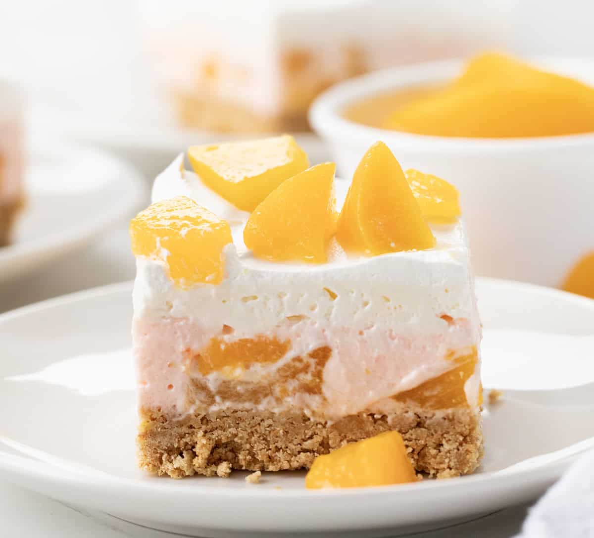 One piece of Peach Delight Dessert on a white plate with more in background.