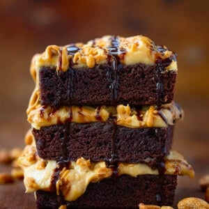 Stack of Peanut Butter Mousse Brownies on a wooden table surrounded by peanuts.