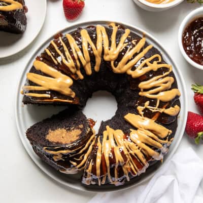 Peanut Butter and Jelly Bundt Cake on a white cake plate with one piece removed and one tipped on its side on a white table from overhead.