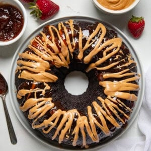 Whole Peanut Butter and Jelly Bundt Cake on a white cake plate on a white table from overhead.