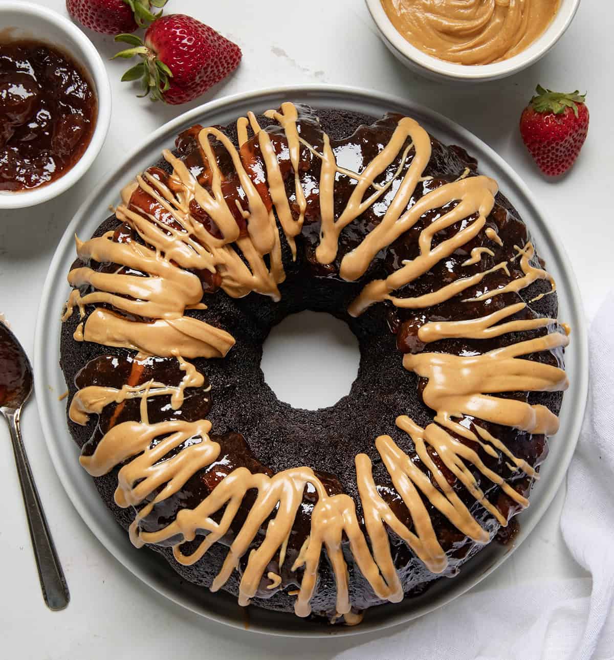 Whole Peanut Butter and Jelly Bundt Cake on a white cake plate on a white table from overhead. 