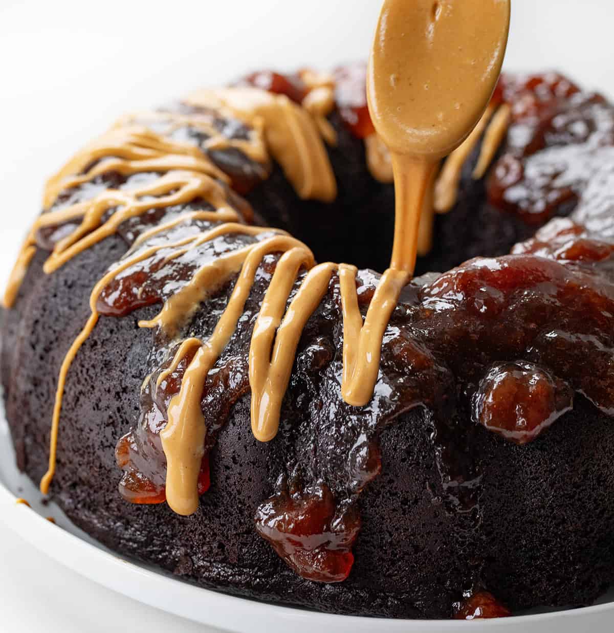 Drizzling peanut butter over jelly on a chocolate bundt cake with peanut butter hidden inside.