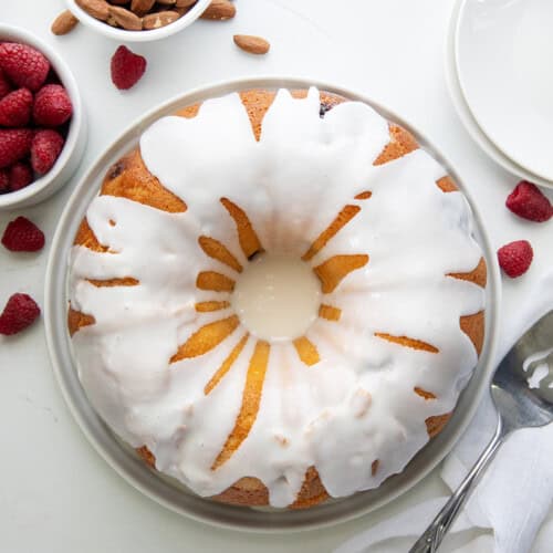 Raspberry Almond Pound Cake on a white cake plate on a white table from overhead.