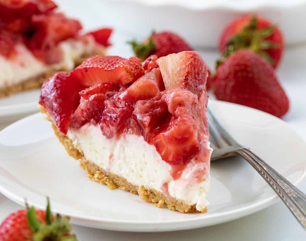 Piece of pie on a white plate with a fork and surrounded by strawberries.