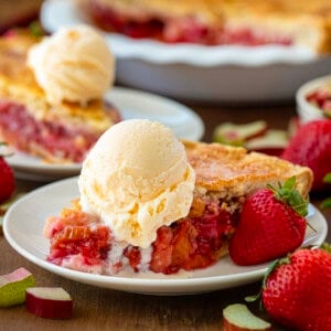Pieces of Strawberry Rhubarb Pie on plates on a wooden table with strawberries around.
