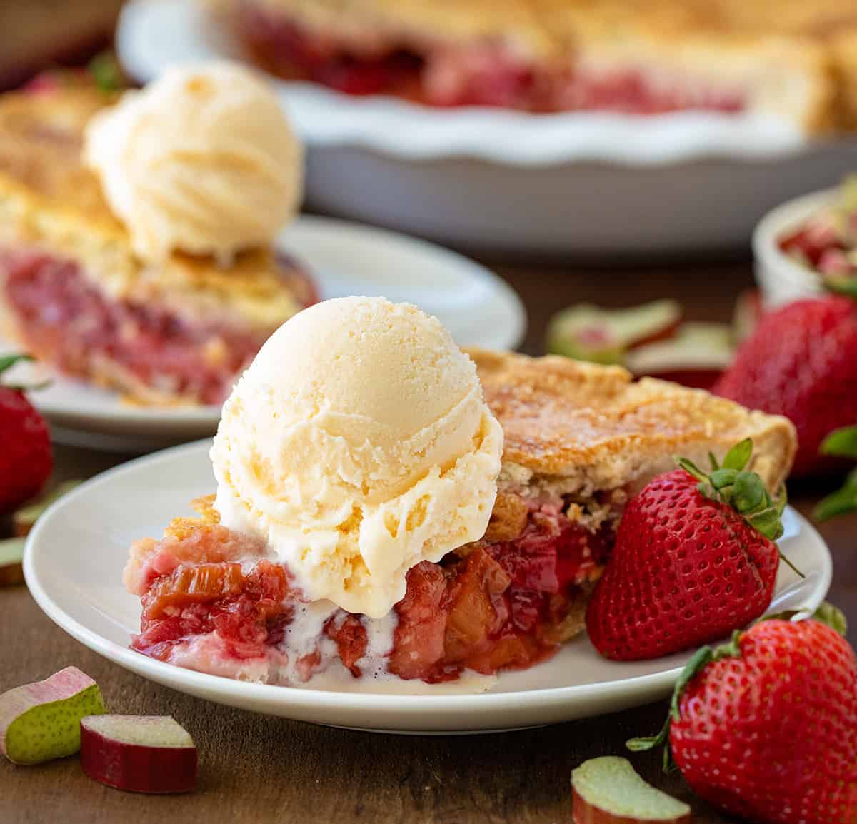 Pieces of Strawberry Rhubarb Pie on plates on a wooden table with strawberries around.