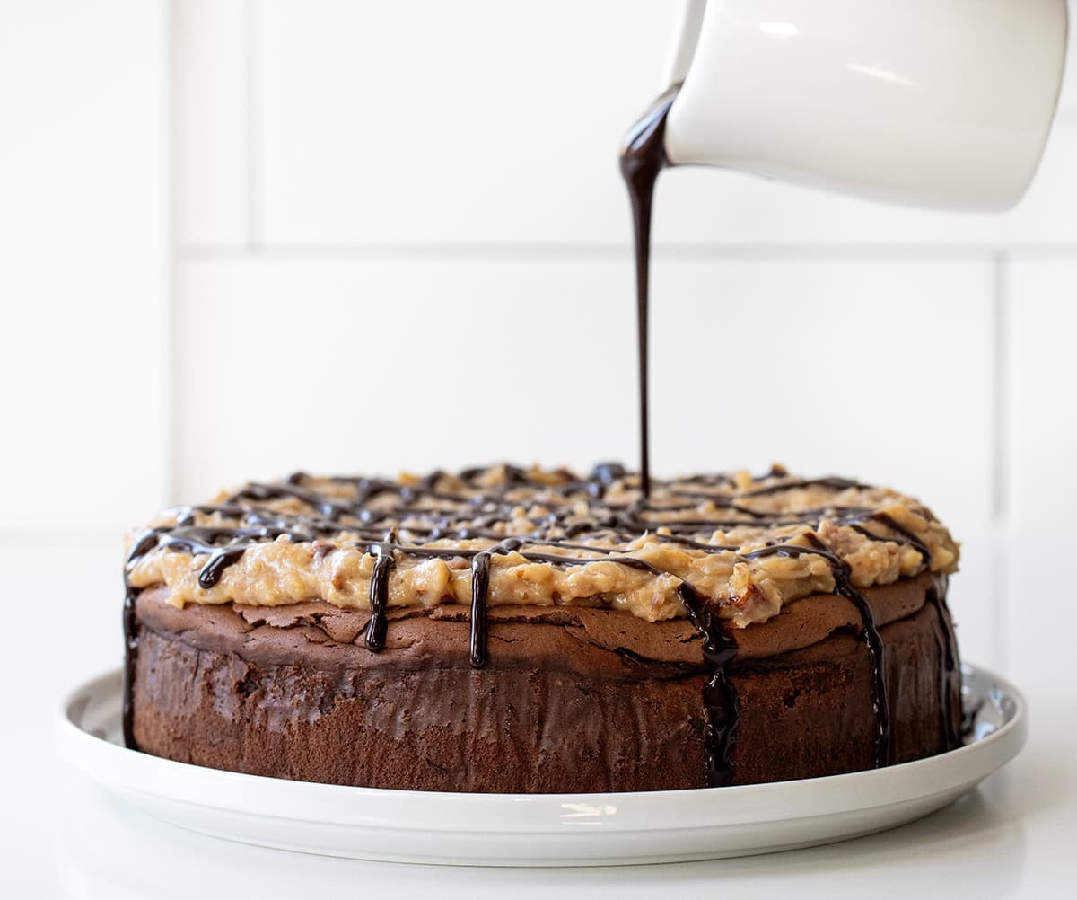 Drizzling chocolate sauce over German Chocolate Cheesecake on a white counter.