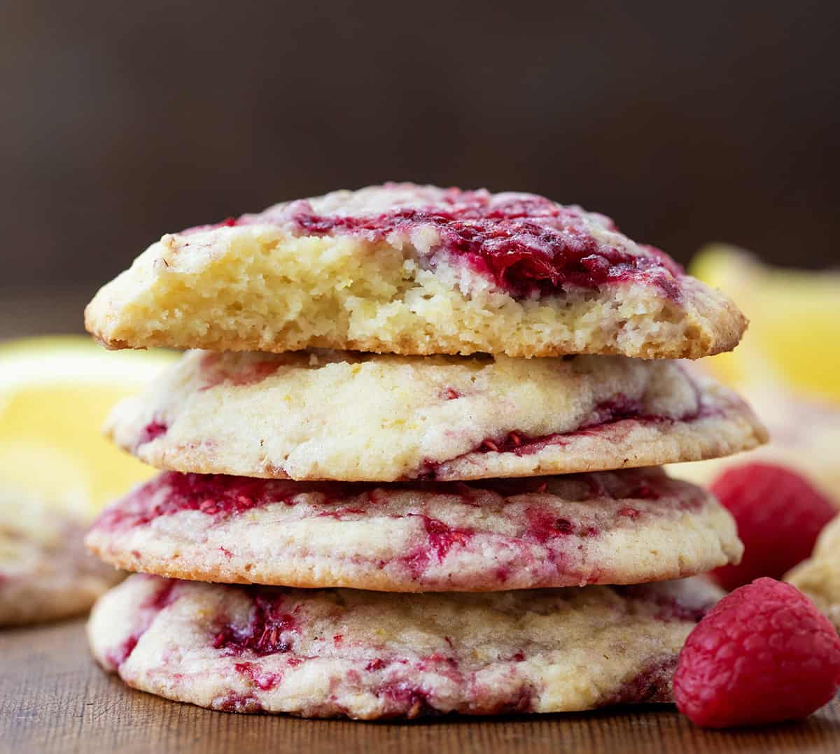 Stack of Lemon Raspberry Cookies on a wooden table straight on with top cookie halved showing inside texture.
