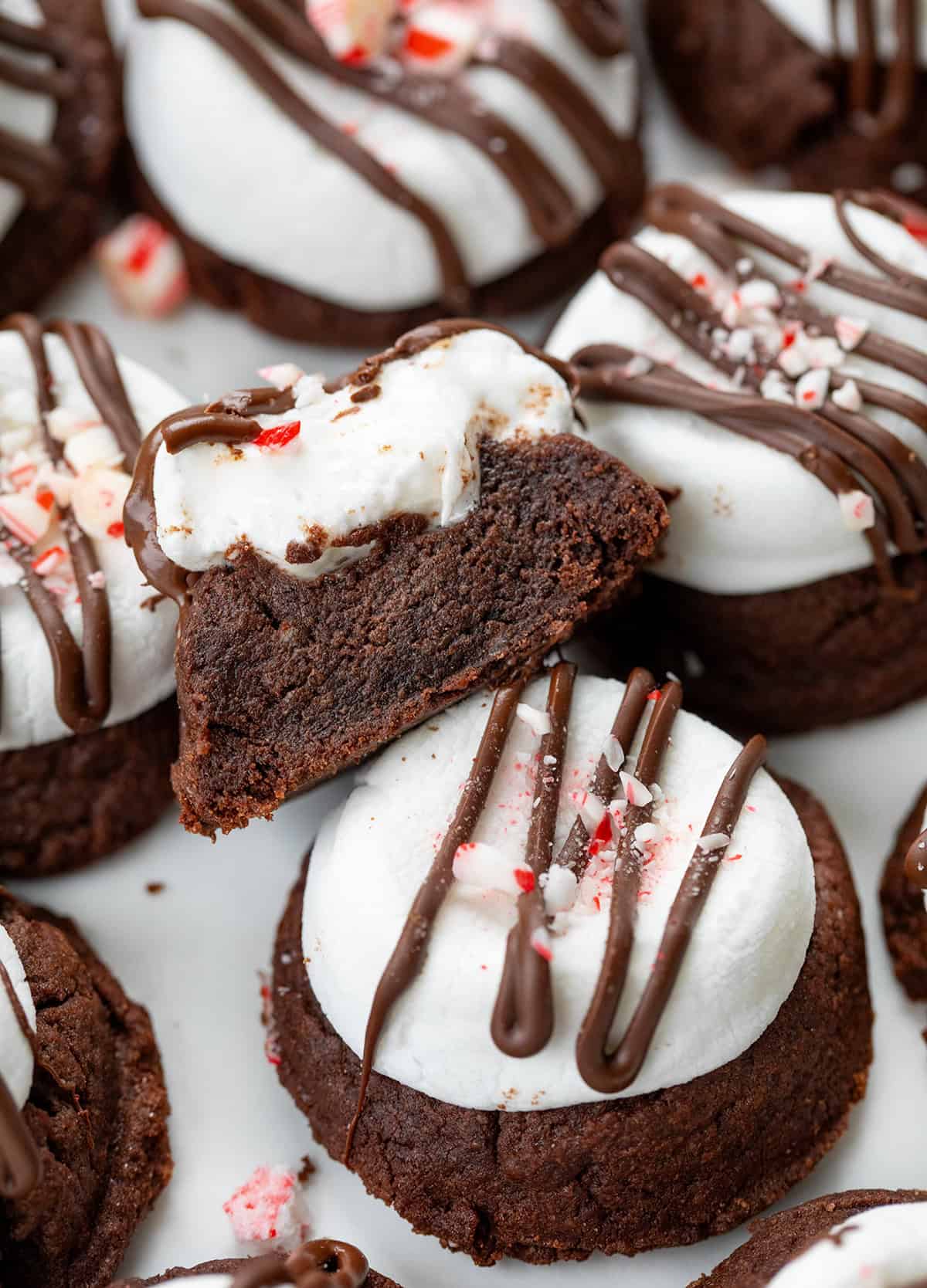 Scattered Peppermint Hot Chocolate Cookies on a white counter with one cookie cut in half.