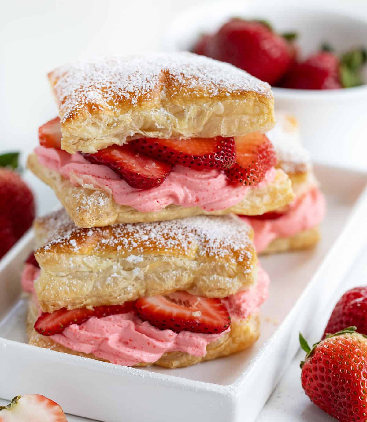 Strawberry Cheesecake Napoleon stacked on itself and dusted with confectioners sugar in a white dish. 