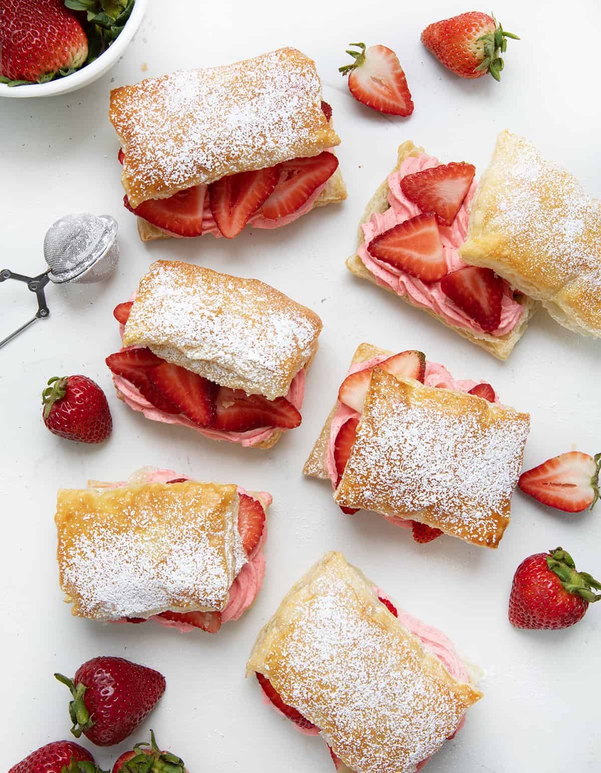 Several Strawberry Cheesecake Napoleons on a white table with strawberries and confectioners sugar.