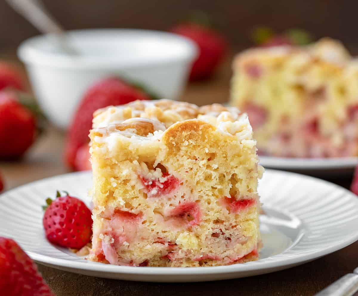 One piece of Strawberry Crumb Cake on a white plate on a wooden table close up with strawberries around.