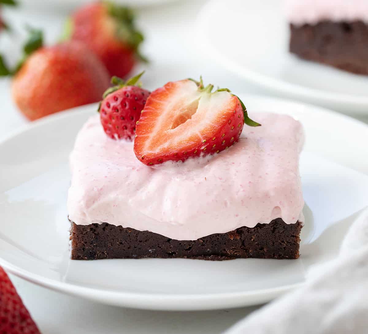 One Strawberry Mousse Brownie on a white plate with mousse spilling over and a strawberry on top.