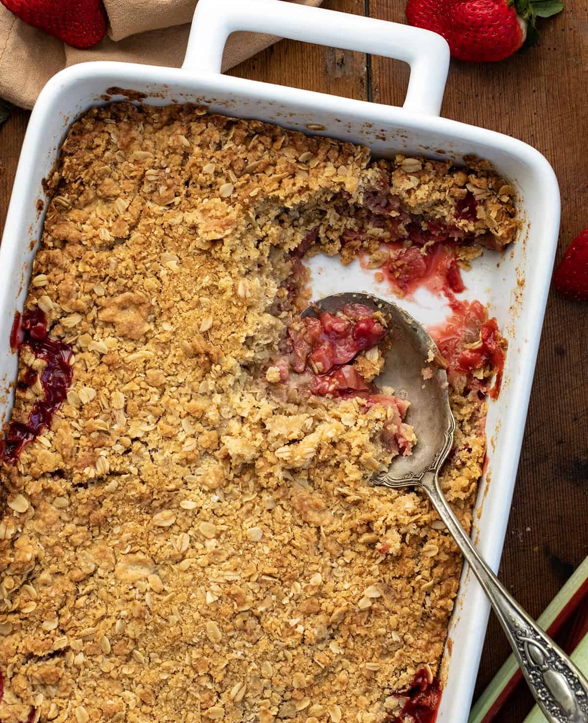 Pan of Strawberry Rhubarb Crisp with a portion removed and a spoon in the pan from overhead.