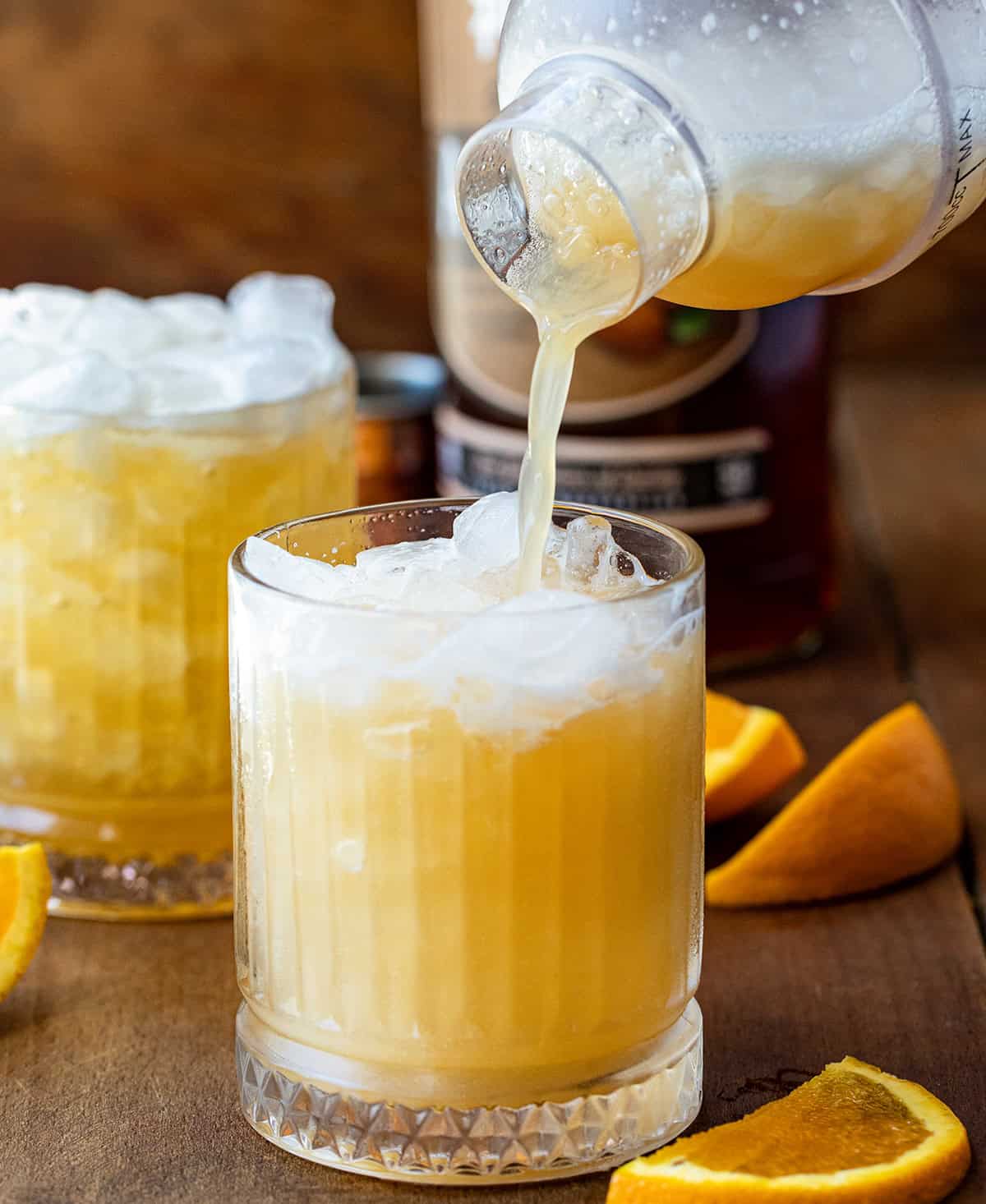 Pouring the Amaretto Sour cocktail into a glass with ice.