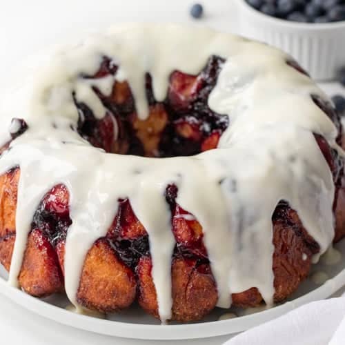 Blueberry Monkey Bread with a Vanilla Glaze on a white plate on a white counter.