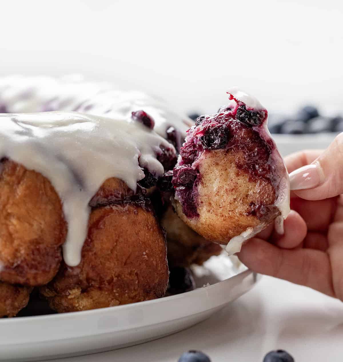 Hand picking up a piece of Blueberry Monkey Bread from the plate.