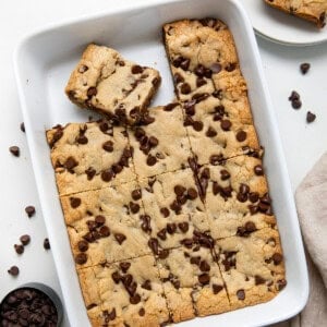 Pan of Brown Butter Chocolate Chip Bars on a white table with a napkin and a measuring cup of chocolate chips from overhead.