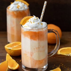 Two Dirty Orange Creamsicle Floats on a wooden table with fresh orange slices around.