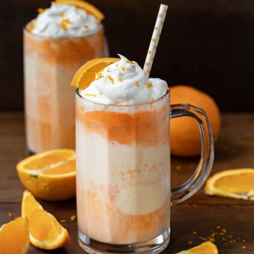 Two Dirty Orange Creamsicle Floats on a wooden table with fresh orange slices around.