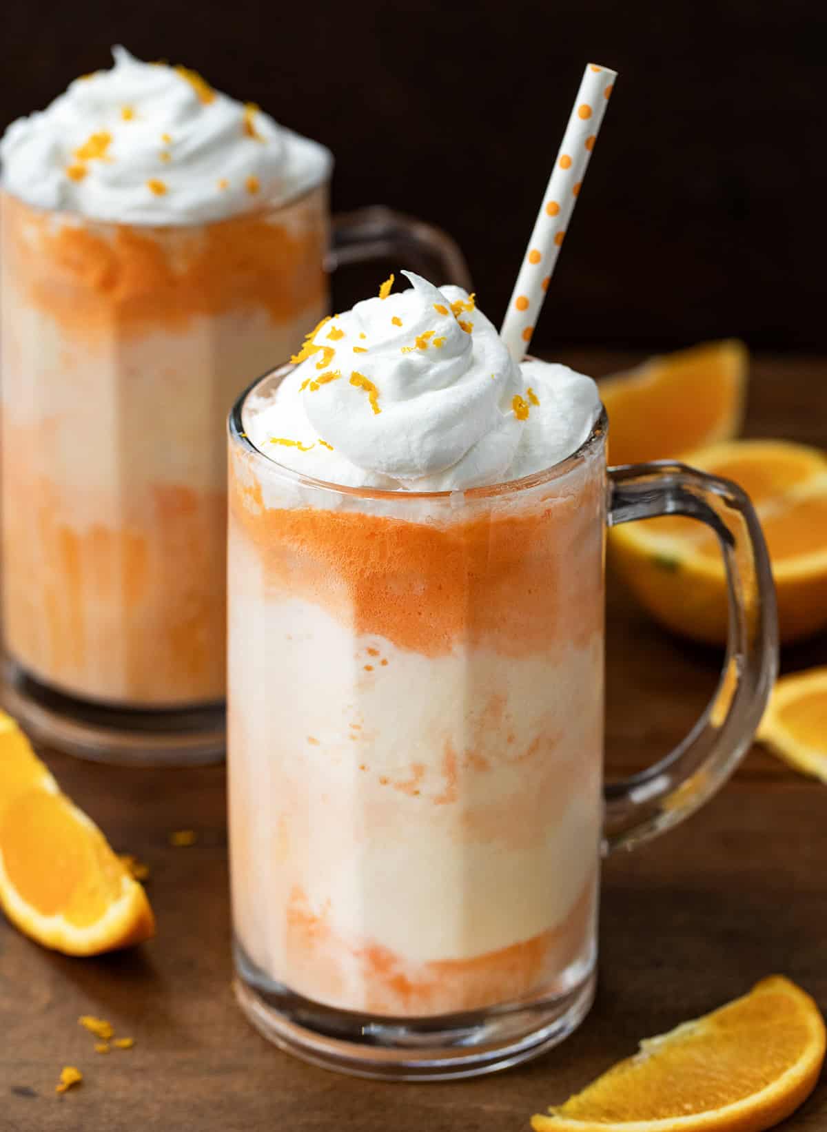 Two Dirty Creamsicle Floats on a wooden table with fresh orange slices around.