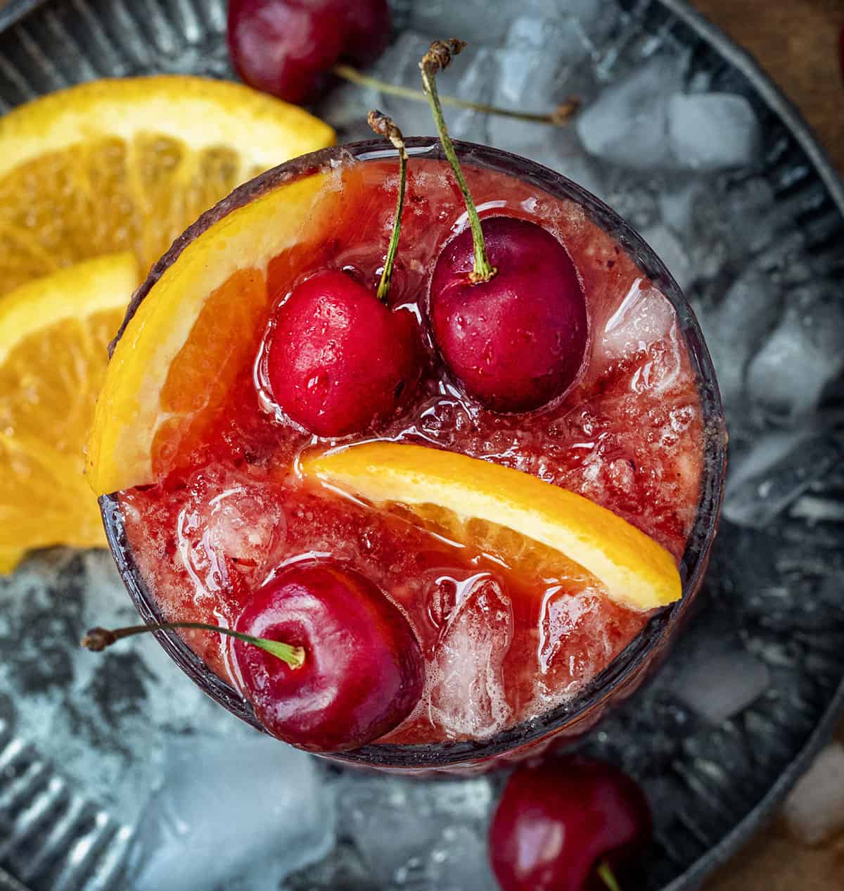 Looking down into a glass of Frozen Old Fashioned with orange slices and fresh cherries.