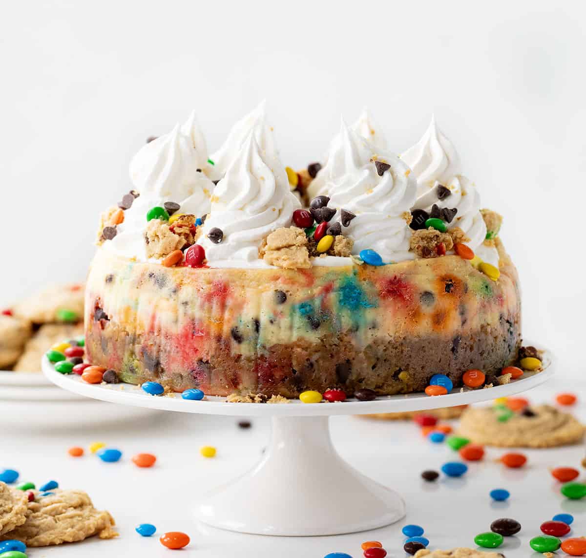 Monster Cookie Cheesecake on a white cake stand with M&M's and cookies around it.