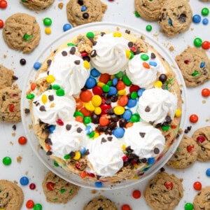 Monster Cookie Cheesecake on a cake stand on a white table surrounded by monster cookies.