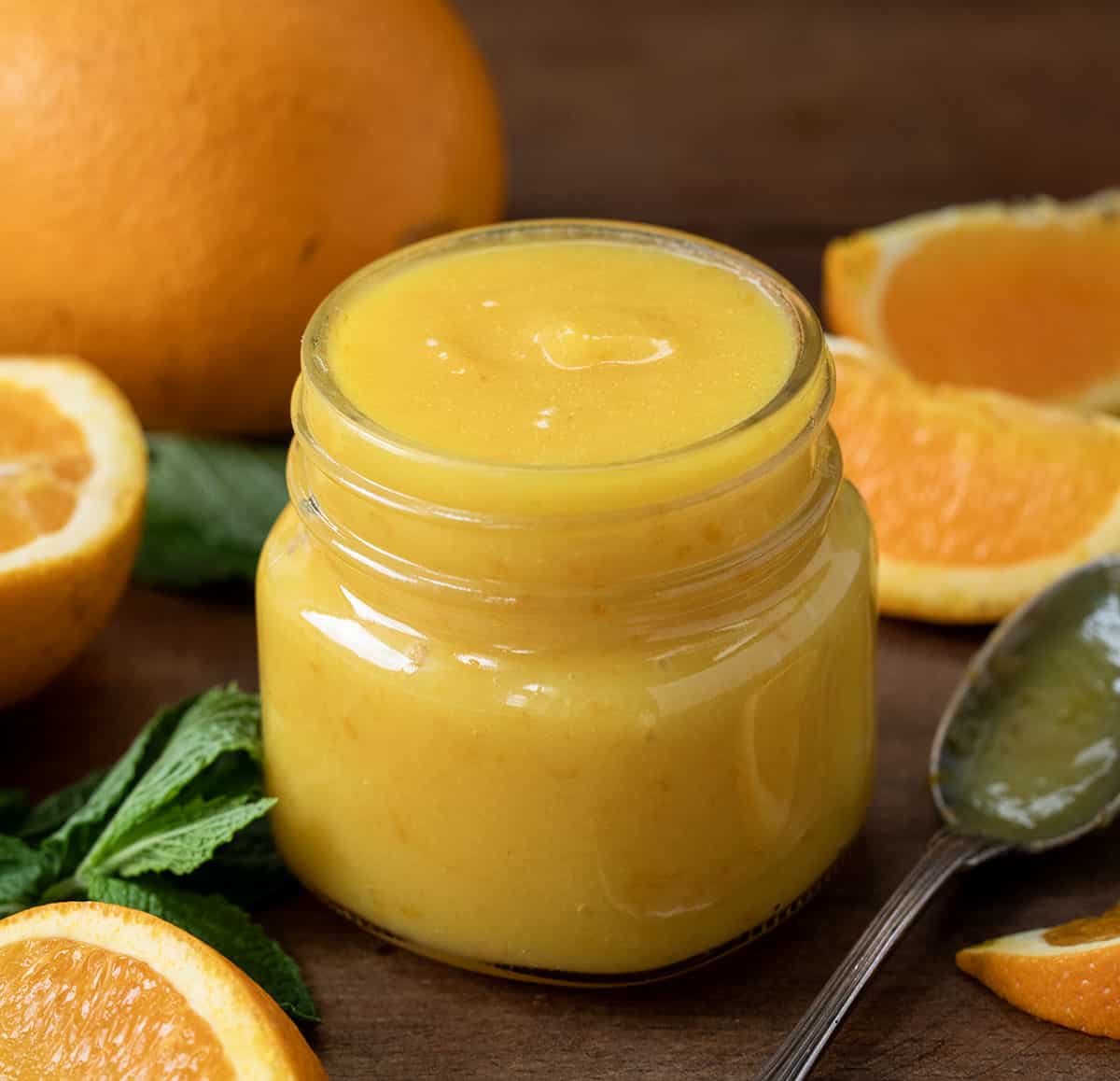 Jar of Orange Curd on a wooden table surrounded by fresh cut oranges. 