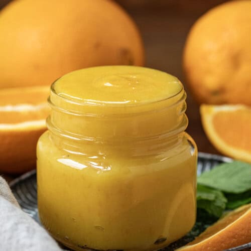 Jar of Orange Curd on a wooden table surrounded by fresh cut oranges.