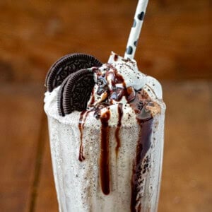 CLose up of the top of an Oreo Milkshake with Oreo and hot fudge and a straw.