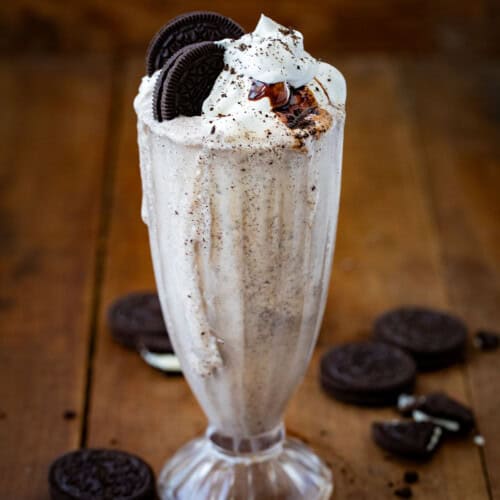 Oreo Milkshake on a wooden table with oreo and whipped cream and hot fudge.