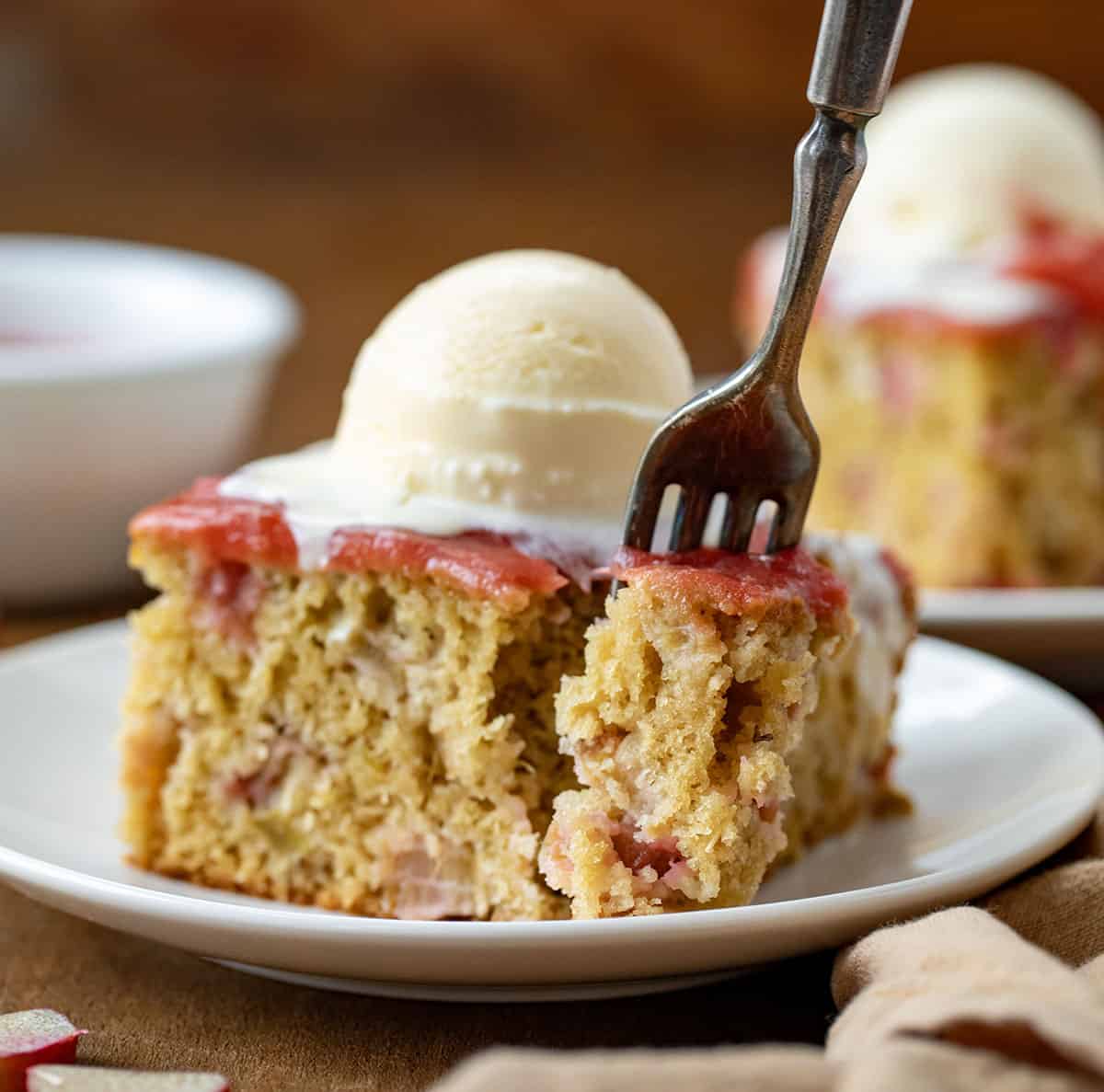 Fork taking a bite out of a piece of Rhubarb Cake With Rhubarb Sauce on a white plate.