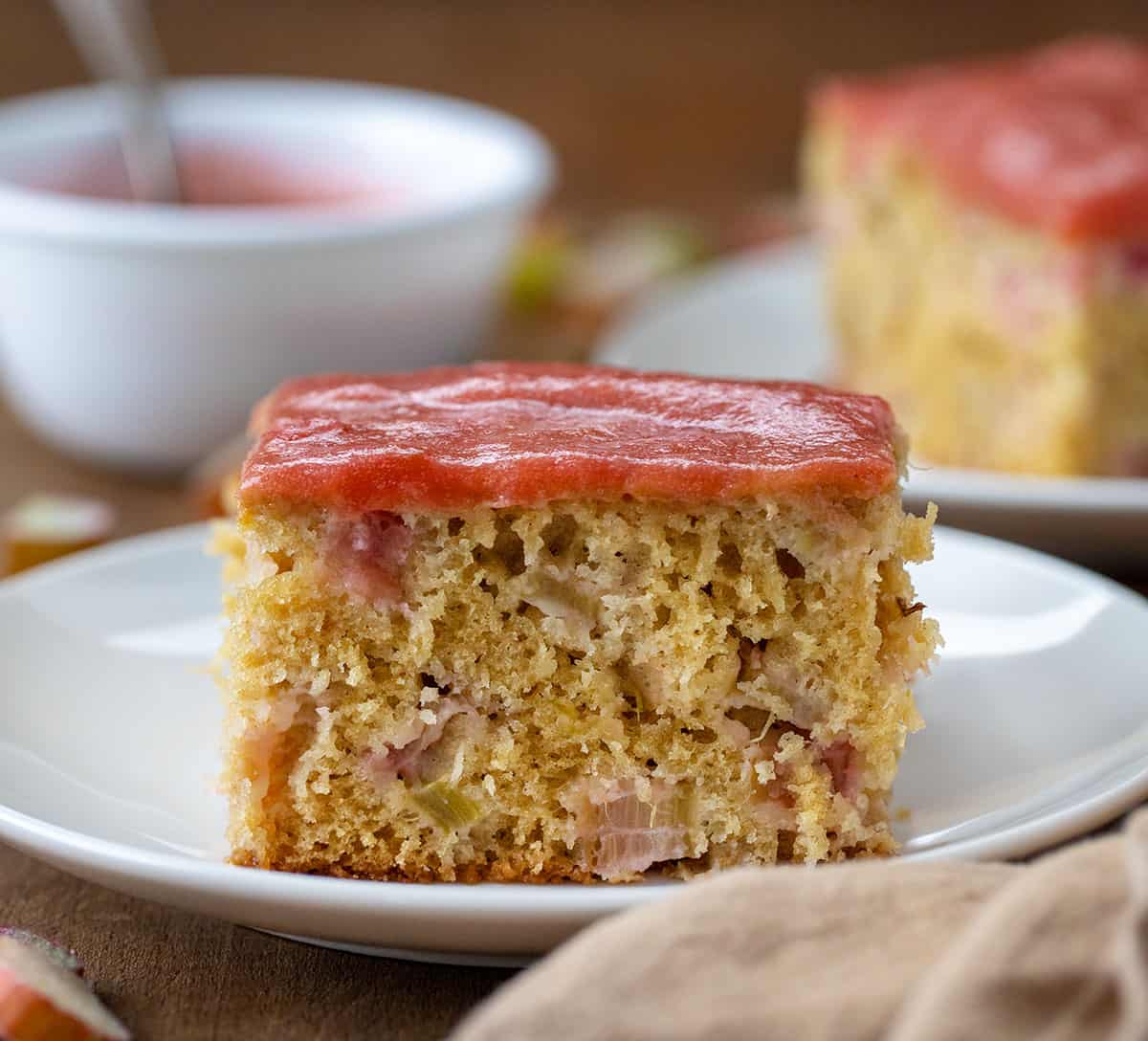 Piece of Rhubarb Cake on a white plate on a wooden table.