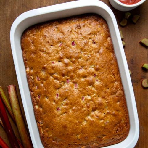 Whole Rhubarb Cake on a wooden table with Rhubarb Sauce off to the side from overhead.