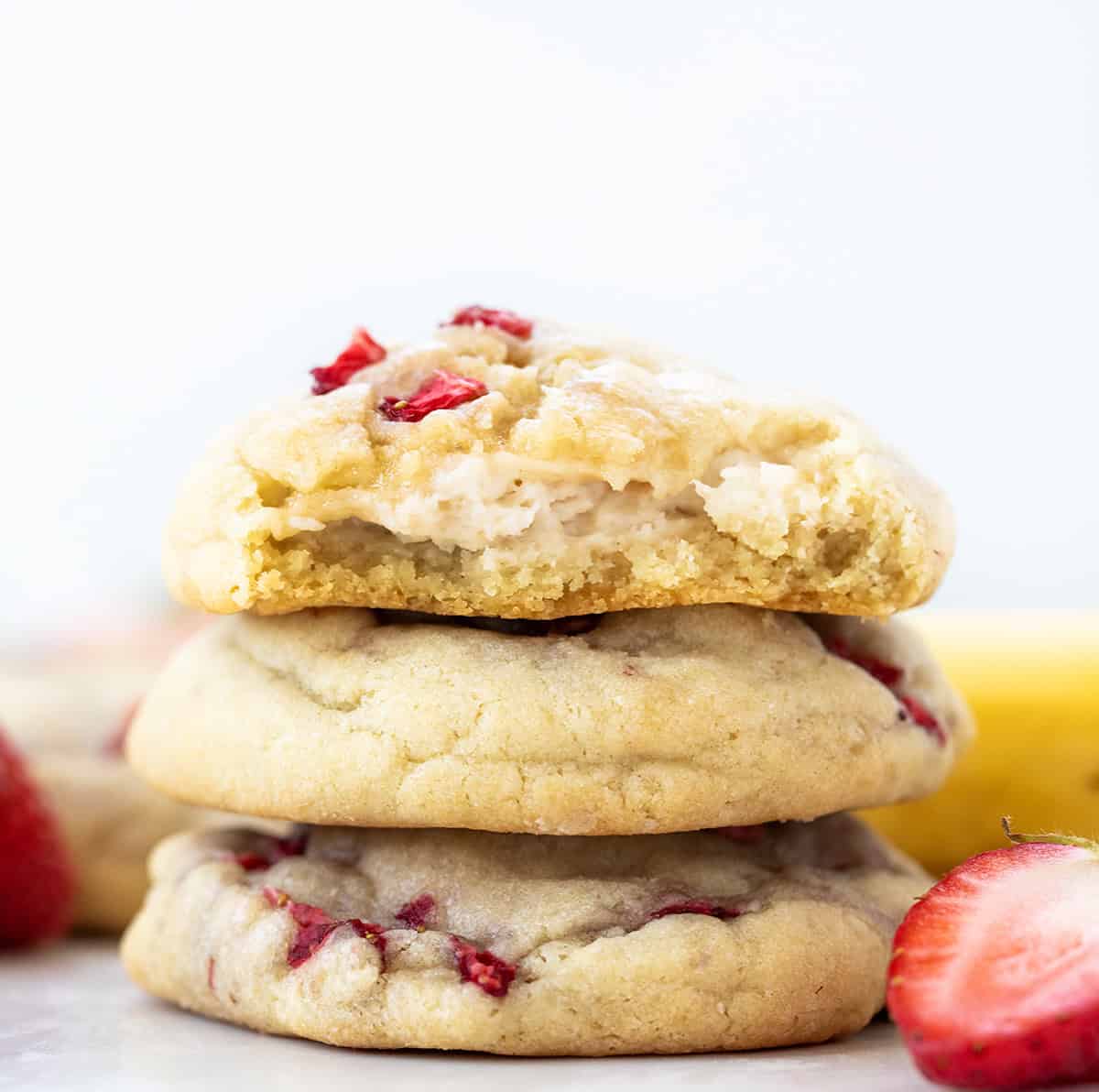 Stack of Strawberry Banana Cheesecake Cookies with one broken in half showing cheesecake inside. 