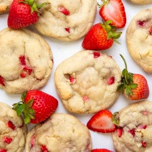 Strawberry Banana Cheesecake Cookies on a white table surrounded by strawberries and a banana.