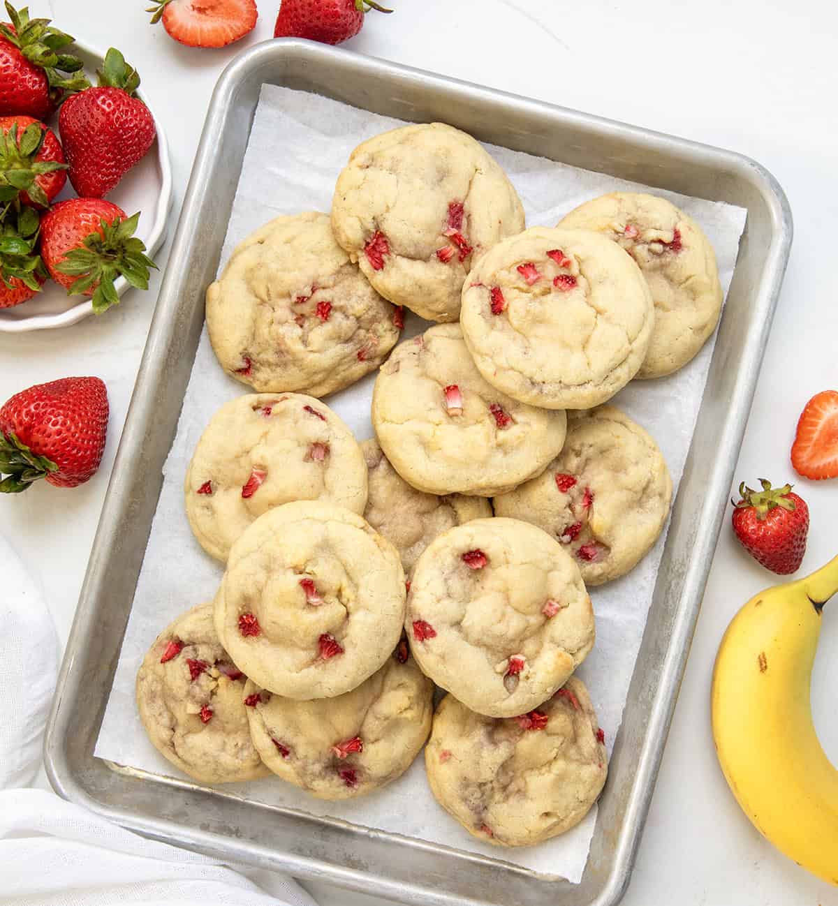 Strawberry Banana Cheesecake Cookies on a white table surrounded by strawberries and a banana.