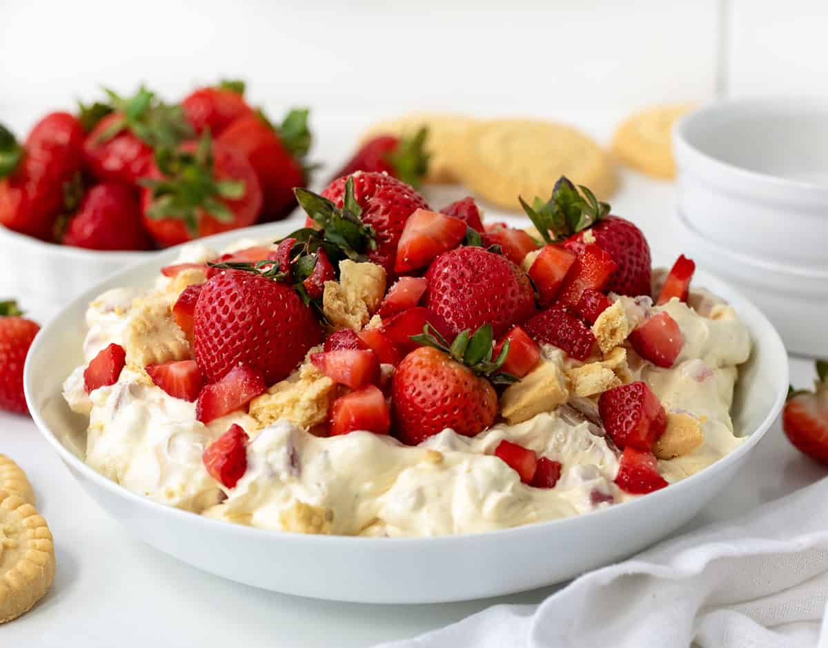 Strawberry Shortcake Cookie Salads in bowls on a white counter surrounded by shortbread cookies and strawberries.