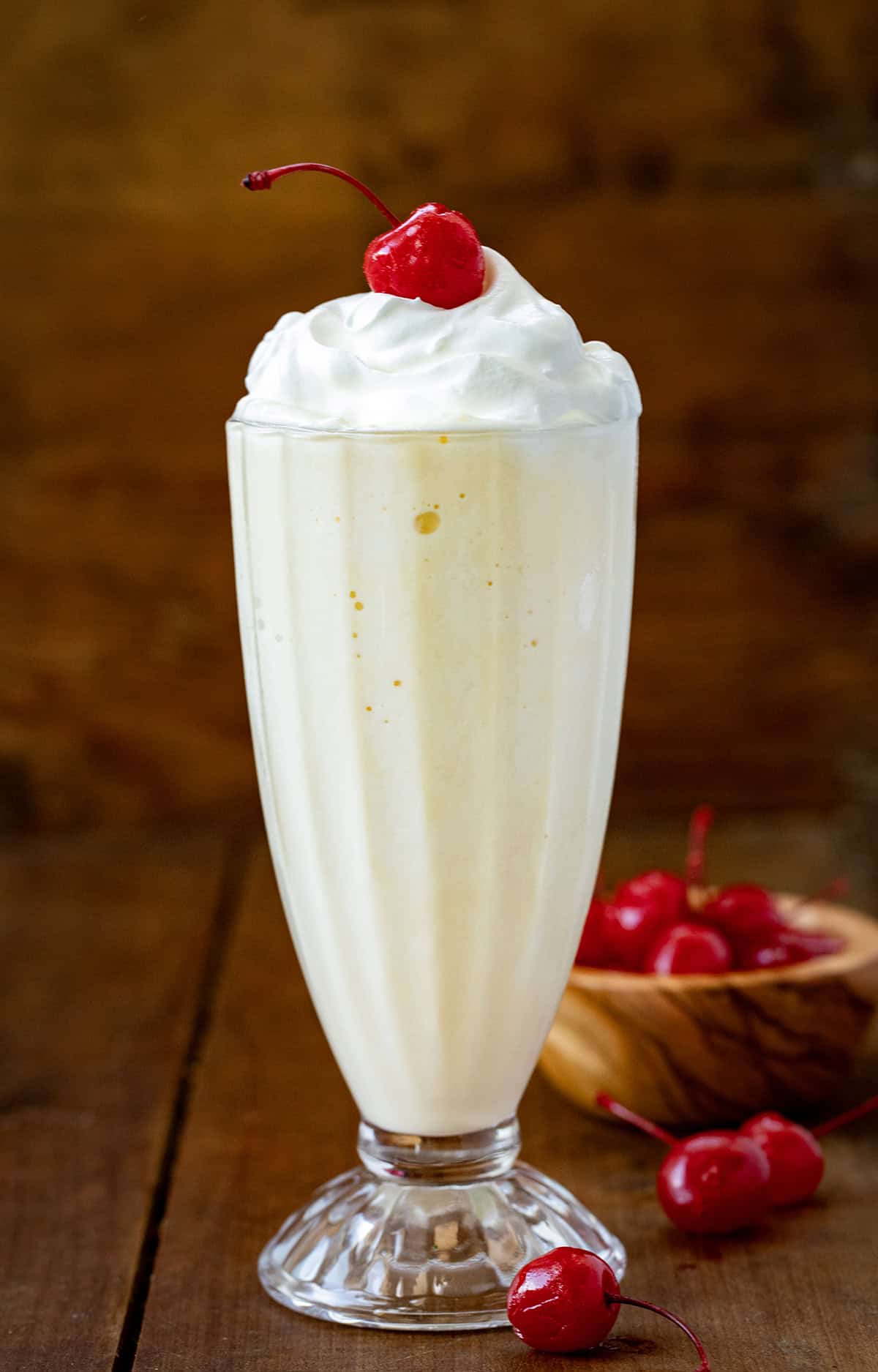 Vanilla Milkshake on a wooden table with whipped cream and cherries. 