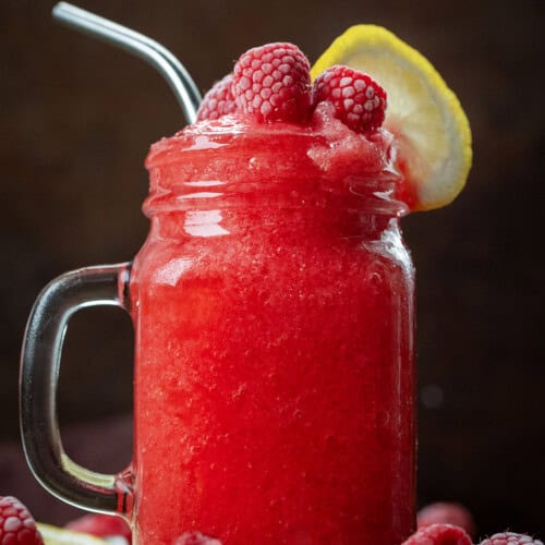 Glass of Frozen Raspberry Lemonade with frozen raspberries and fresh lemon.