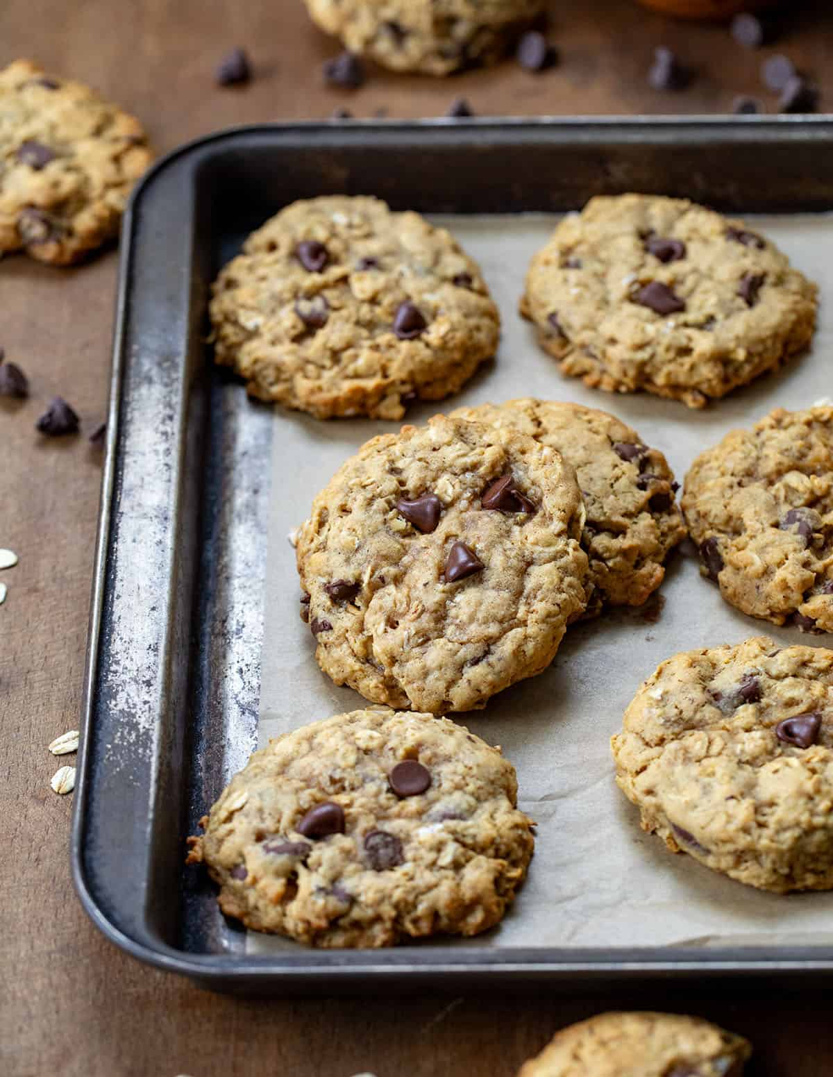 Brown Butter Oatmeal Chocolate Chip Cookies on a baking sheet with parchment paper on a wooden table.