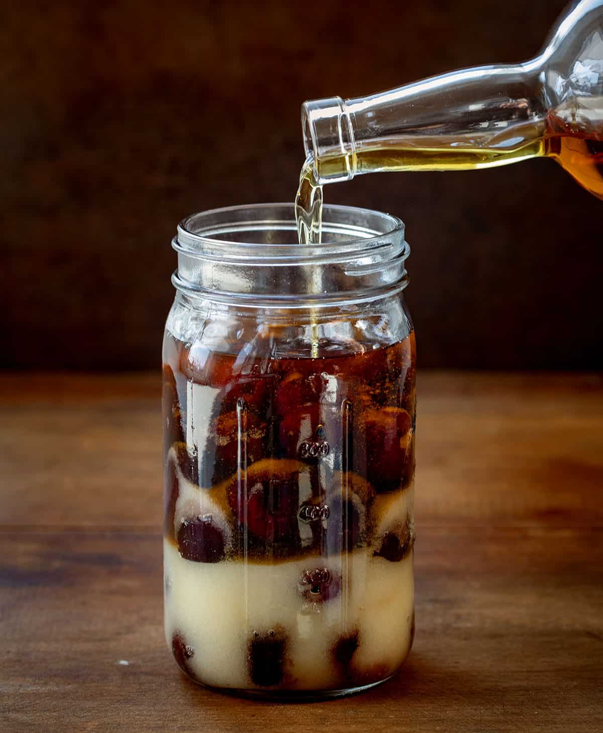 Adding liquor to jar of cherries and sugar.